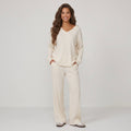 Woman wearing cream 2-piece ribbed knit loungewear set with V-neck long-sleeve top and straight-leg trousers